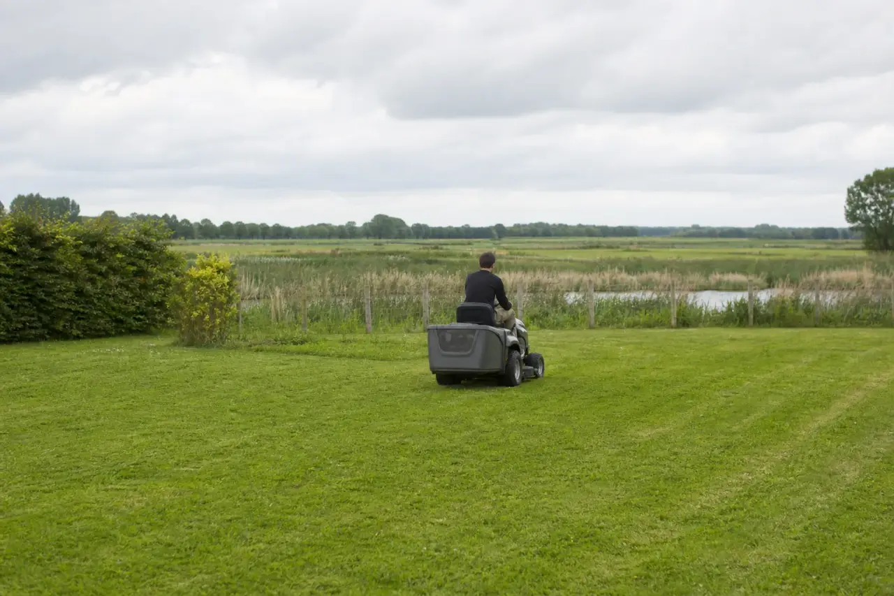 Jardinier passant la tondeuse autoportée sur une grande pelouse de la plaine berrichonne, ciel bas et horizon dégagé de l'Indre.